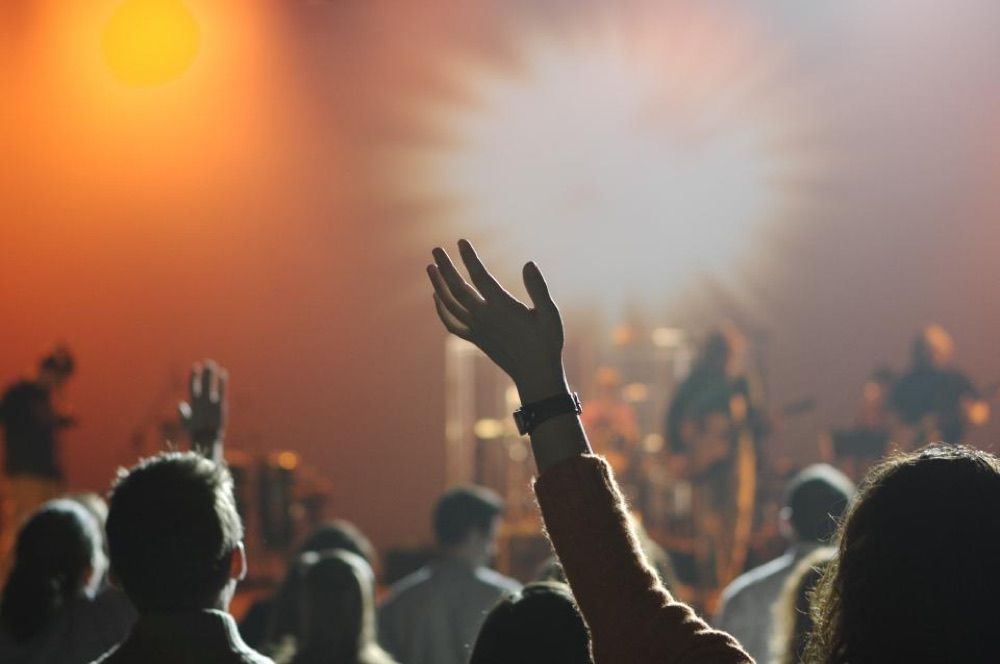 A concert crowd in low light, hands raised in front of a bright stage